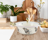 Decorative bowl with floral patterns on a kitchen counter with plants and wooden cutting boards.