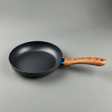 A dark gray non-stick frying pan with a light brown wooden handle, shown on a neutral gray background.