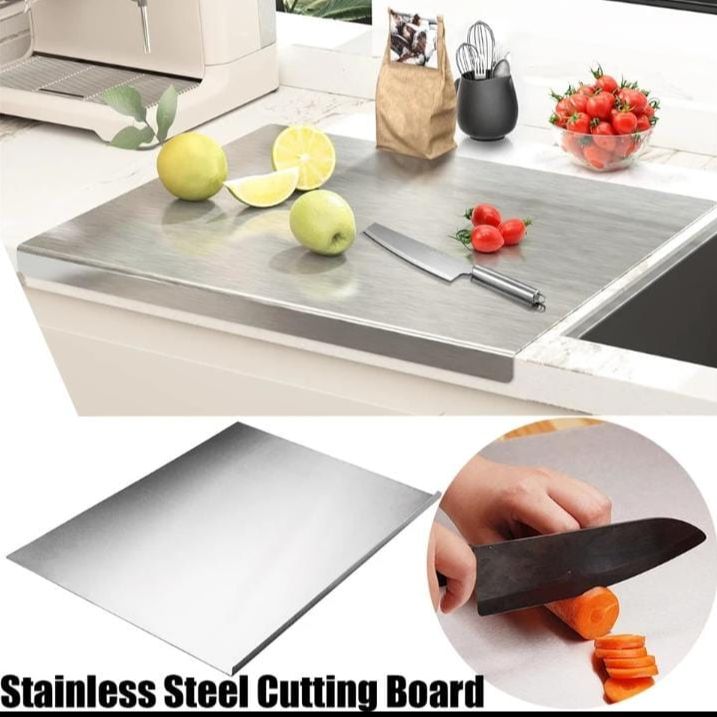 Stainless steel cutting board with knife and vegetables on a kitchen counter, close-up of board, and person cutting carrots.